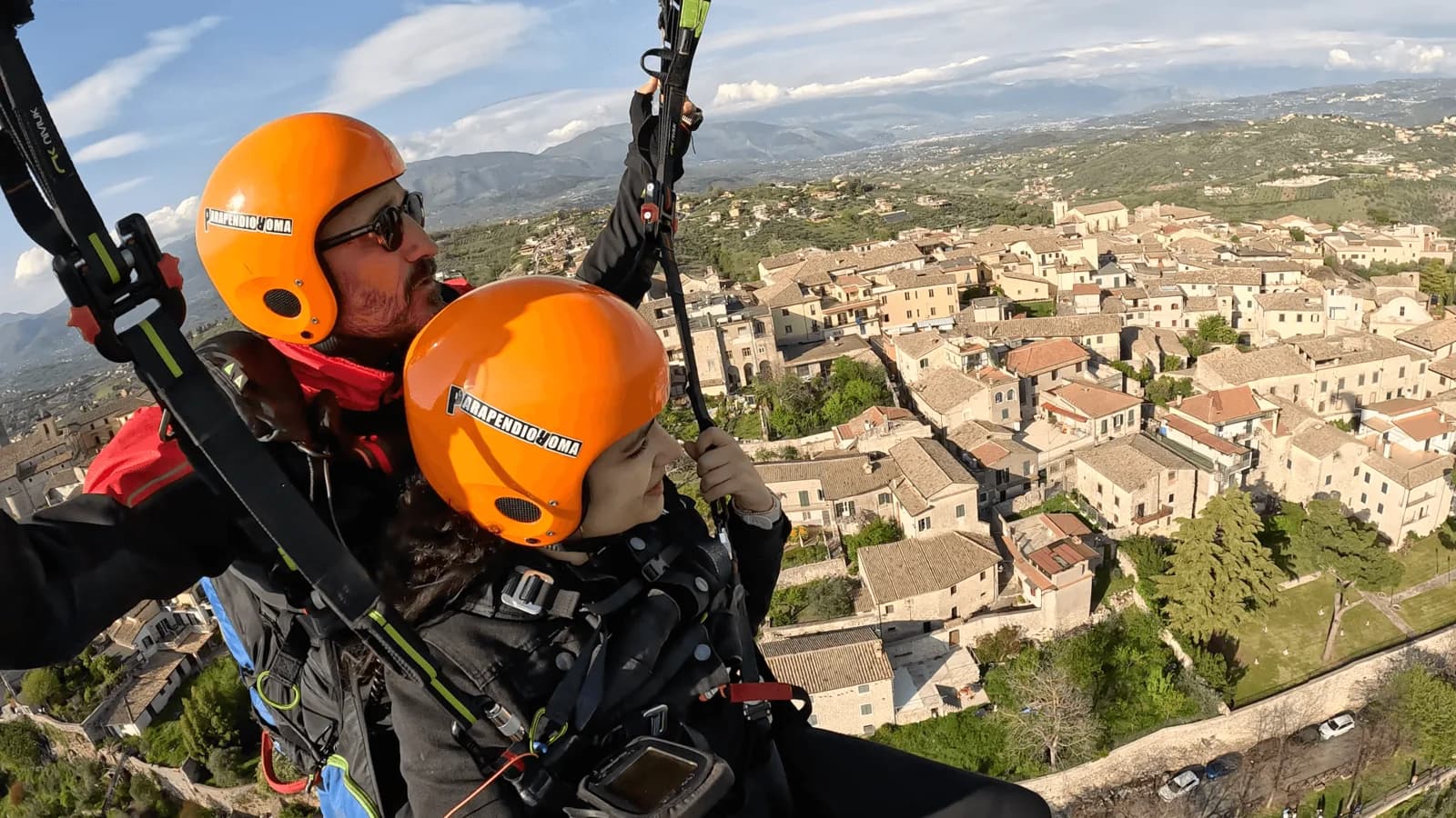 Tandem paraglider flying over a medieval hill town in Lazio